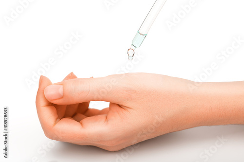 A drop from the pipette drips on a beautiful, well-groomed female hand. Hand skin care product, white background very close-up