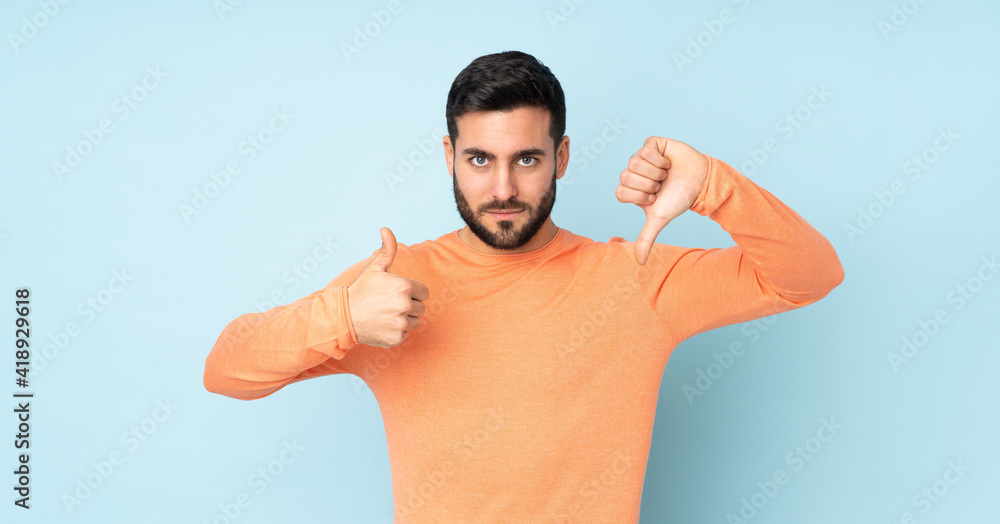 Fototapeta premium Caucasian handsome man making good-bad sign. Undecided between yes or not over isolated blue background