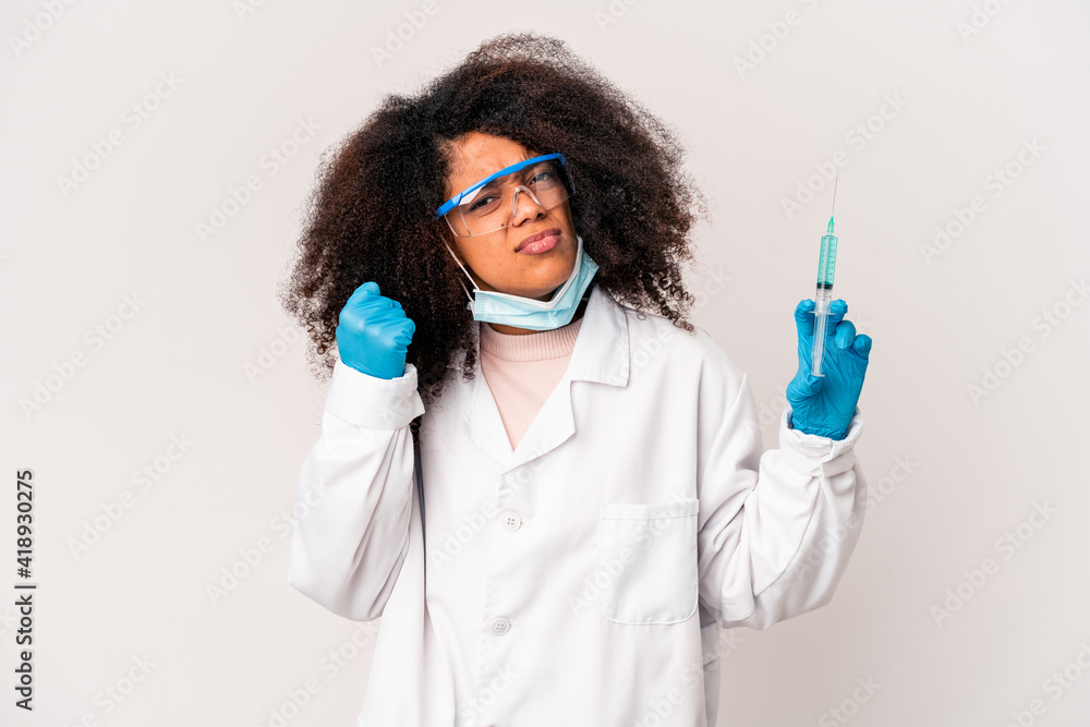 Young african american curly doctor woman holding a syringe showing fist to camera, aggressive facial expression. Young african american curly doctor woman holding a syringe showing fist to camera, aggressive facial expression.