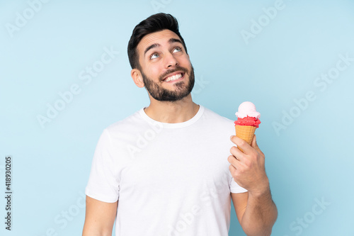 Caucasian man with a cornet ice cream isolated on blue background looking up while smiling