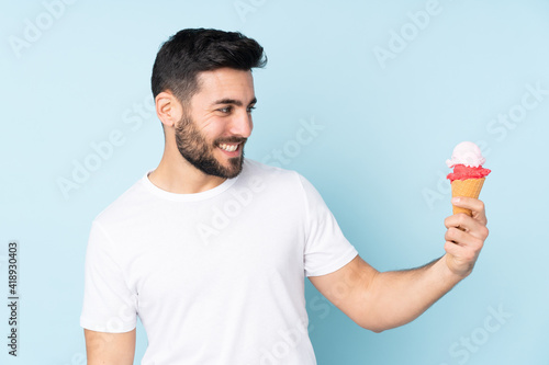Caucasian man with a cornet ice cream isolated on blue background with happy expression