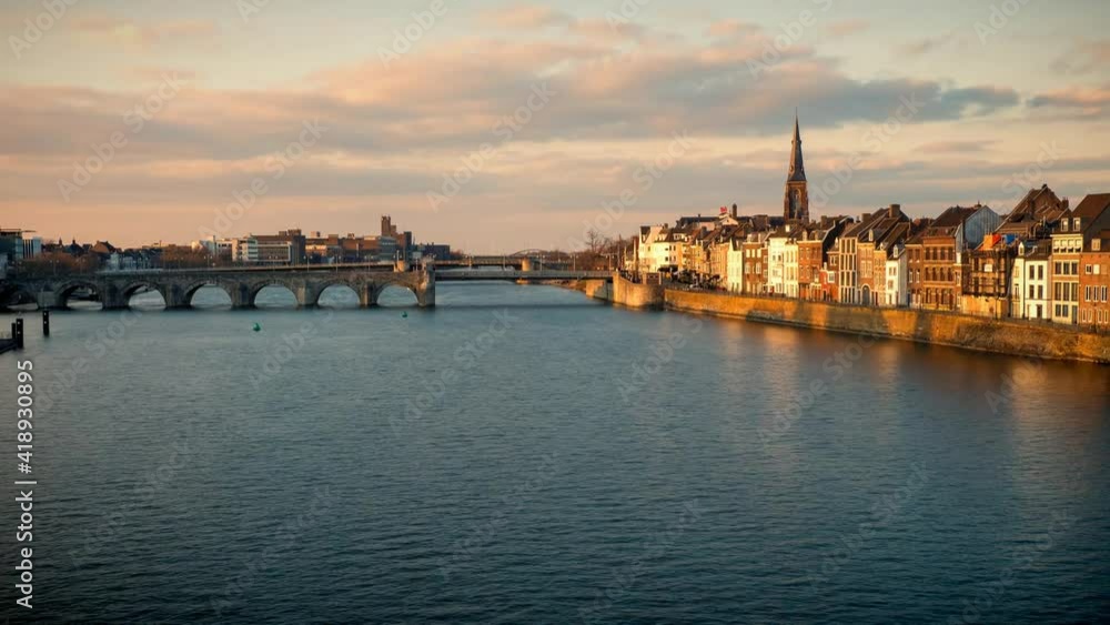 Time lapse view of a beautiful sunset at the waterfront of Maastricht, the Netherlands, with people walking along the promenade in front of old town houses at the river Maas Time lapse view of a beautiful sunset at the waterfront of Maastricht, the Netherlands, with people walking along the promenade in front of old town houses at the river Maas
