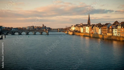 Time lapse view of a beautiful sunset at the waterfront of Maastricht, the Netherlands, with people walking along the promenade in front of old town houses at the river Maas
