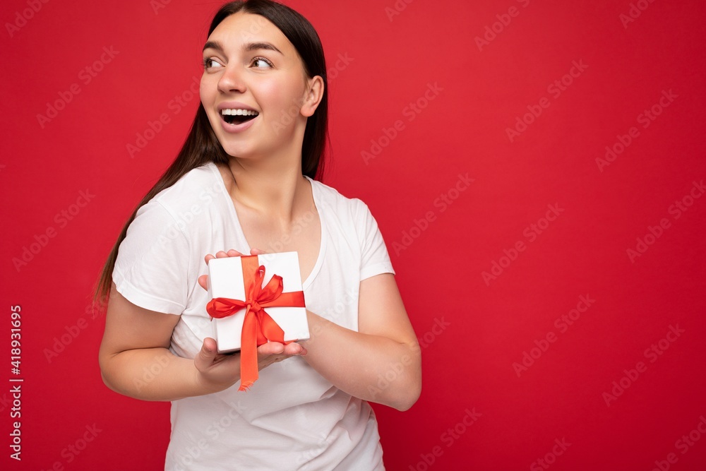 Beautiful happy young brunette woman isolated over colourful background wall wearing stylish casual clothes holding gift box and looking to the side Beautiful happy young brunette woman isolated over colourful background wall wearing stylish casual clothes holding gift box and looking to the side