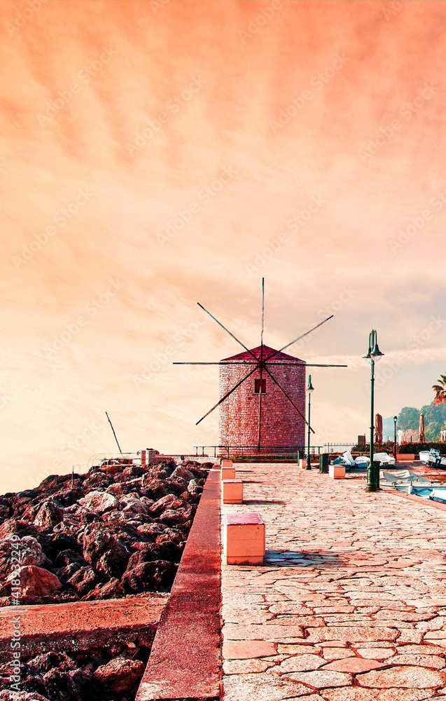 Charming seafront view with stones, lanterns and old windmill on the coast of the Mon Repose area in Kerkira, capital of Corfu, Greece at sunrise. Amazing places. Popular tourist atraction.