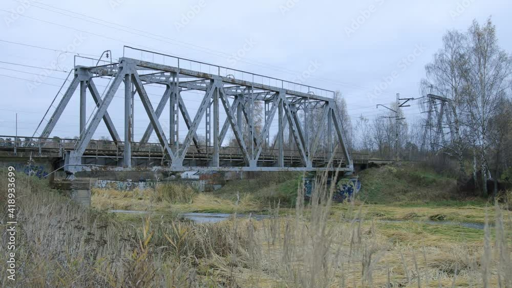Suburban train is crossing the small bridge over water in countryside-like location in Russia. Autumn cloudy weather. Suburban train is crossing the small bridge over water in countryside-like location in Russia. Autumn cloudy weather.