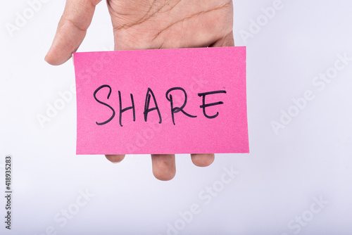 Share word written on a Pink color sticky note in front of a hand with a White background. © GlobalReporter