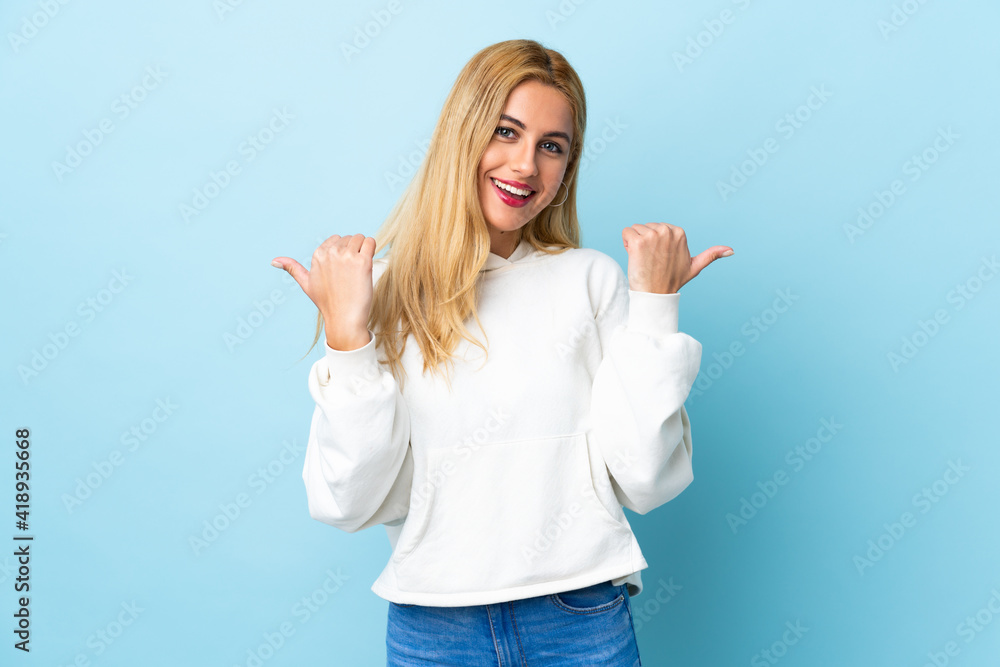 Young Uruguayan blonde woman over isolated blue background with thumbs up gesture and smiling Young Uruguayan blonde woman over isolated blue background with thumbs up gesture and smiling