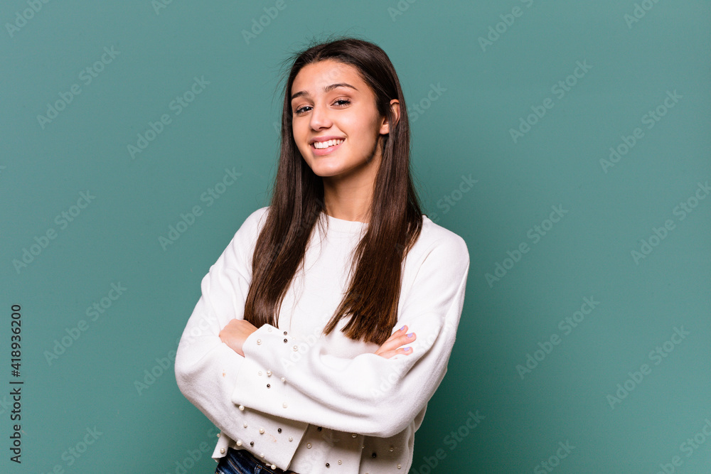Young Indian woman isolated on blue background who feels confident, crossing arms with determination. Young Indian woman isolated on blue background who feels confident, crossing arms with determination.