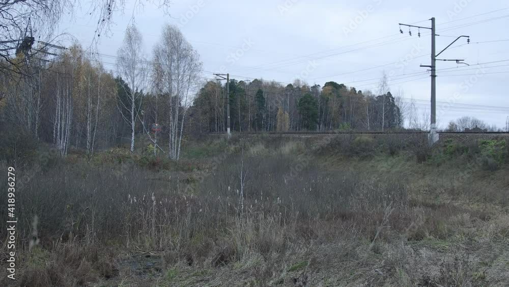 Suburban train is appearing from the woods and crossing the small bridge over water in countryside-like location in Russia. Autumn cloudy weather. Tracking shot from left to right Suburban train is appearing from the woods and crossing the small bridge over water in countryside-like location in Russia. Autumn cloudy weather. Tracking shot from left to right