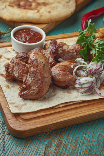 An appetizing oriental dish - grilled pork kebab with a side dish of potatoes and onions with red onions on a green background. Georgian cuisine. Shish kebab