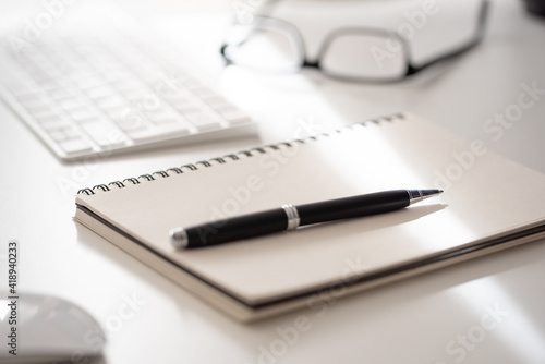 close-up of spiral notepad with ballpoint pen on white office desk, taking notes concept