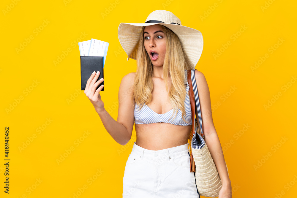 Young Uruguayan blonde woman in swimsuit holding a passport over isolated yellow background with surprise and shocked facial expression Young Uruguayan blonde woman in swimsuit holding a passport over isolated yellow background with surprise and shocked facial expression