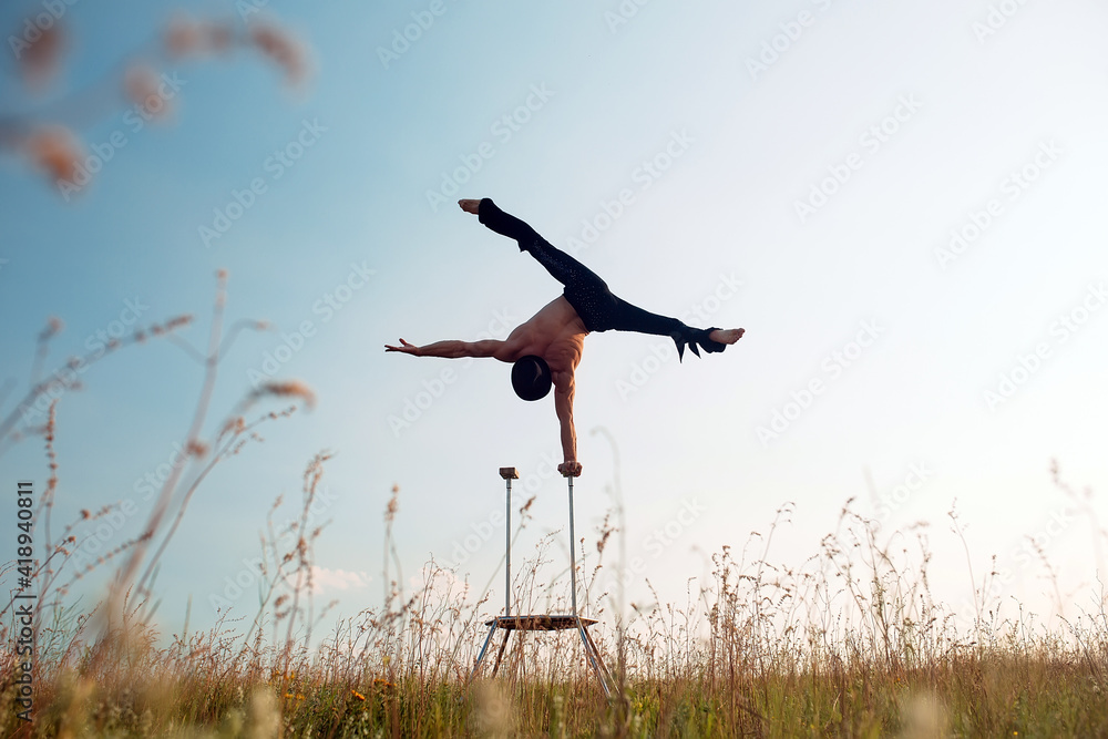 A man of athletic build performs complex gymnastic exercises in a field at sunset.