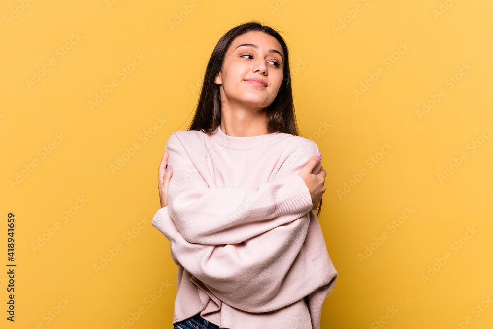 Obraz premium Young Indian woman isolated on yellow background hugs, smiling carefree and happy.