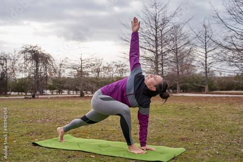 extended side angle yoga pose or utthita parsvakonasana in revolved variation by a woman in a park photo