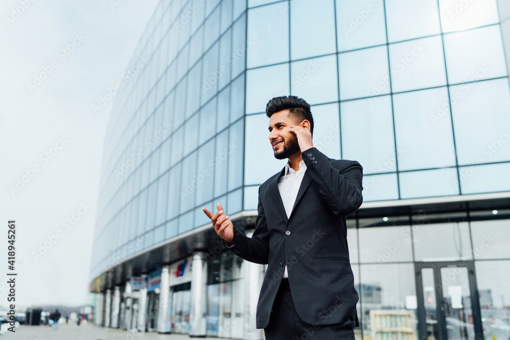 Handsome bearded Indian man talking on the phone, boss, behind him a modern office building Handsome bearded Indian man talking on the phone, boss, behind him a modern office building