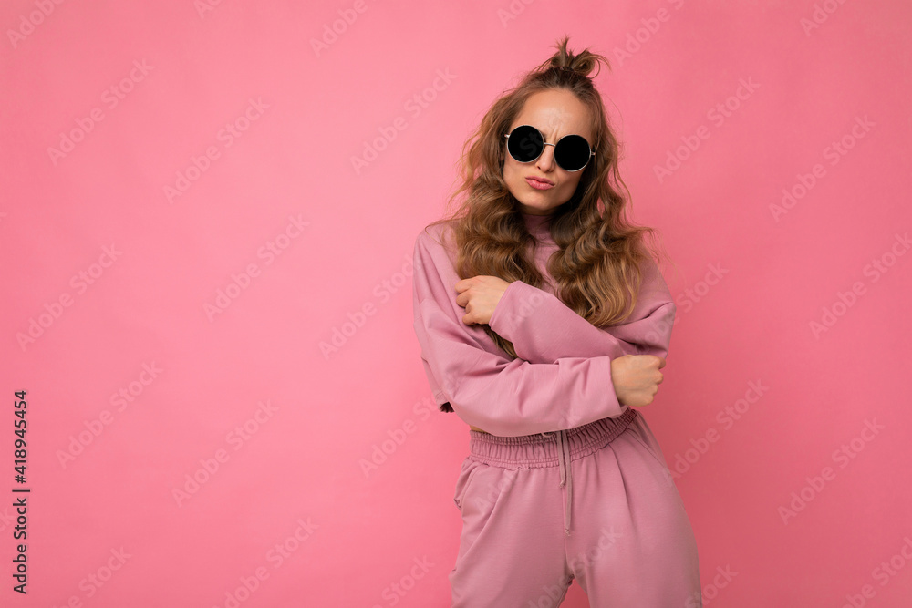 Photo shot of beautiful positive young dark blonde woman wearing casual clothes and stylish sunglasses isolated over colorful background looking at camera Photo shot of beautiful positive young dark blonde woman wearing casual clothes and stylish sunglasses isolated over colorful background looking at camera