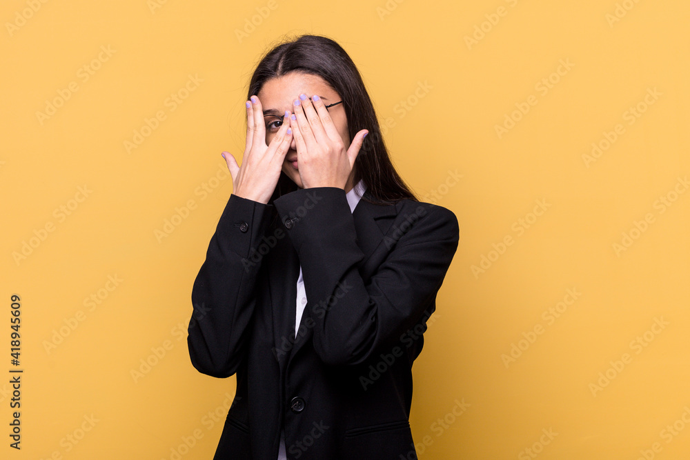 Young Indian business woman isolated on yellow background blink through fingers frightened and nervous. Young Indian business woman isolated on yellow background blink through fingers frightened and nervous.