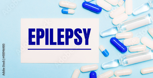 Pills, ampoules and a white card with the text EPILEPSY on a light blue background. Medical concept