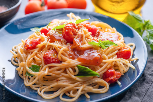 Tasty appetizing classic italian spaghetti pasta with tomato sauce, cheese parmesan and basil on plate and ingredients for cooking pasta on dark table.