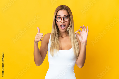 Young blonde woman isolated on yellow background showing ok sign and thumb up gesture