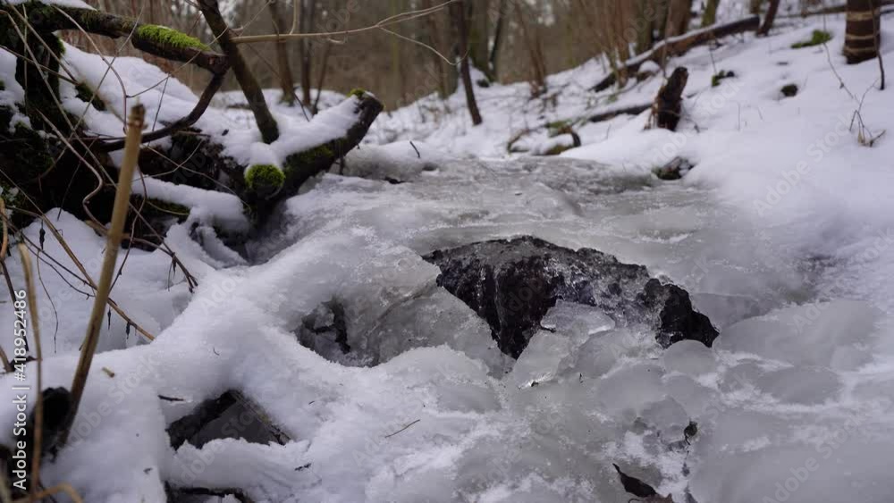 creek flowing under ice in a wood covered with snow in winter, slow jib up creek flowing under ice in a wood covered with snow in winter, slow jib up