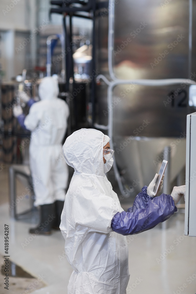 Vertical side view portrait of female worker wearing protective suit while operating equipment at chemical plant Vertical side view portrait of female worker wearing protective suit while operating equipment at chemical plant