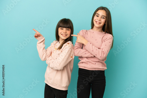 Little sisters girls isolated on blue background pointing finger to the side in lateral position