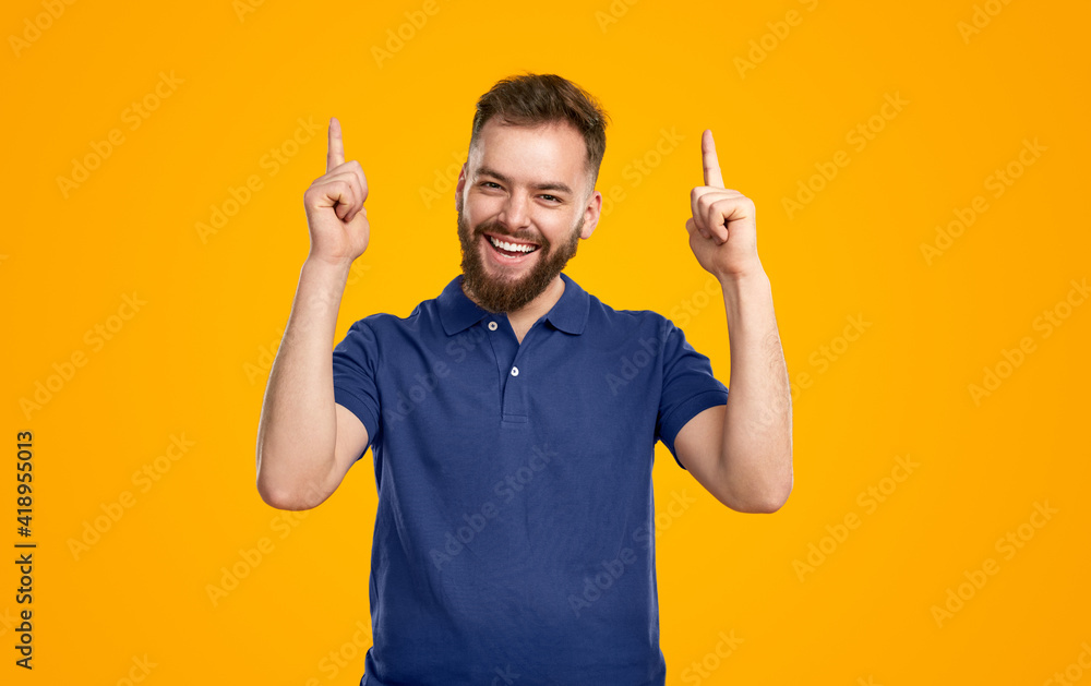 Cheerful young man gesturing forefingers up and smiling at camera