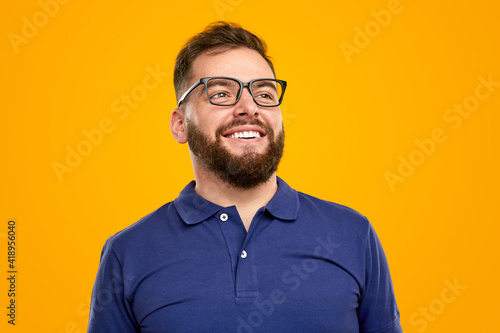 Happy young man smiling and looking away in yellow studio