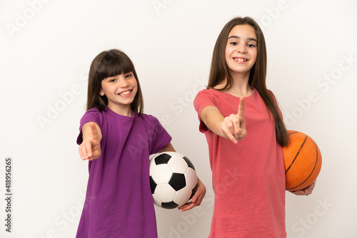 Little sisters playing football and basketball isolated on white background showing and lifting a finger