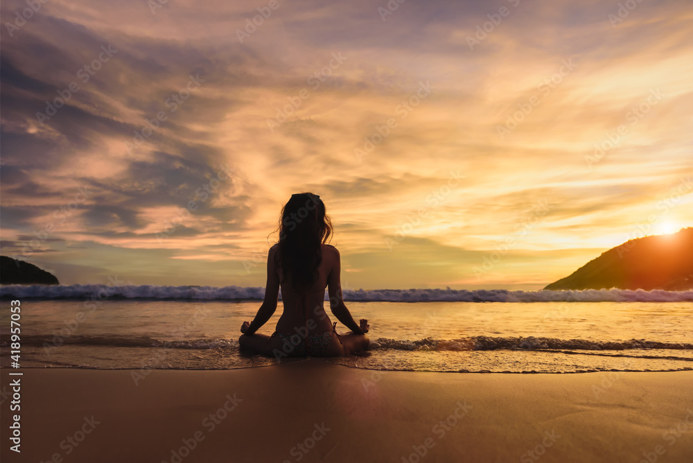 Silhouette of young woman wearing a bikini practicing yoga on the beach at sunset with around sea beach ocean, Yoga Meditation Sunset on the beach alone, Mindfulness Meditation for health.