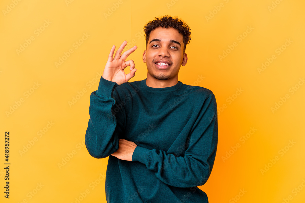 Young african american curly man isolated on purple winks an eye and holds an okay gesture with hand. Young african american curly man isolated on purple winks an eye and holds an okay gesture with hand.