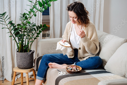 Foto Happy young woman sewing in comforts of her apartment, embroiders a picture
