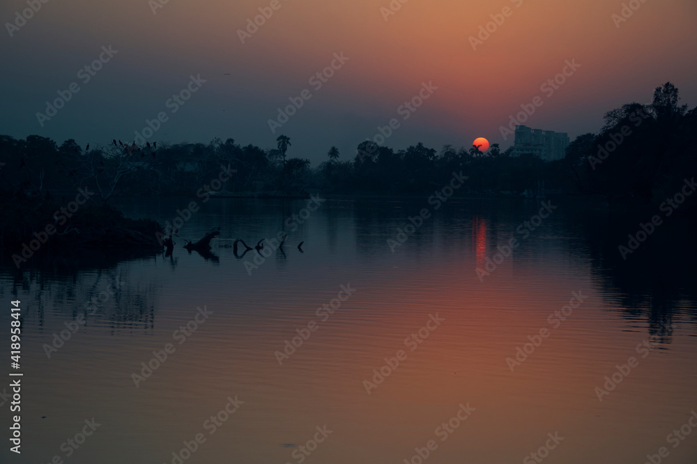 A beautiful sunset at Rabindra Sarobar Lake in Kolkata, with reflection of golden looking sun in lake water.