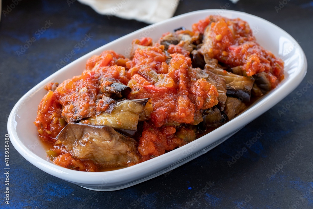Grilled eggplant salad appetizer with tomato sauce (with eggplant sauce or saksuka). Traditional Middle Eastern meze beside the main course. Layout on dark wood Grilled eggplant salad appetizer with tomato sauce (with eggplant sauce or saksuka). Traditional Middle Eastern meze beside the main course. Layout on dark wood