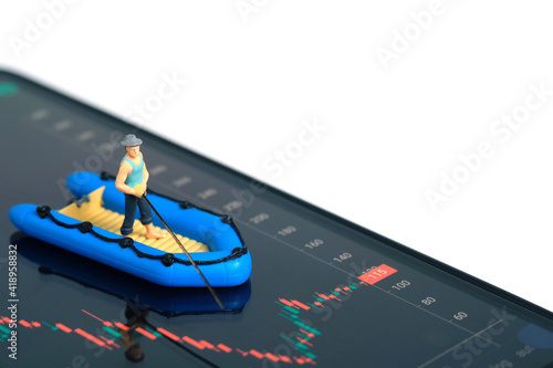 Miniature people toy photography. An angler standing above rubber boat searching investment profit, opened candle chart from stock market app. Isolated on white background.