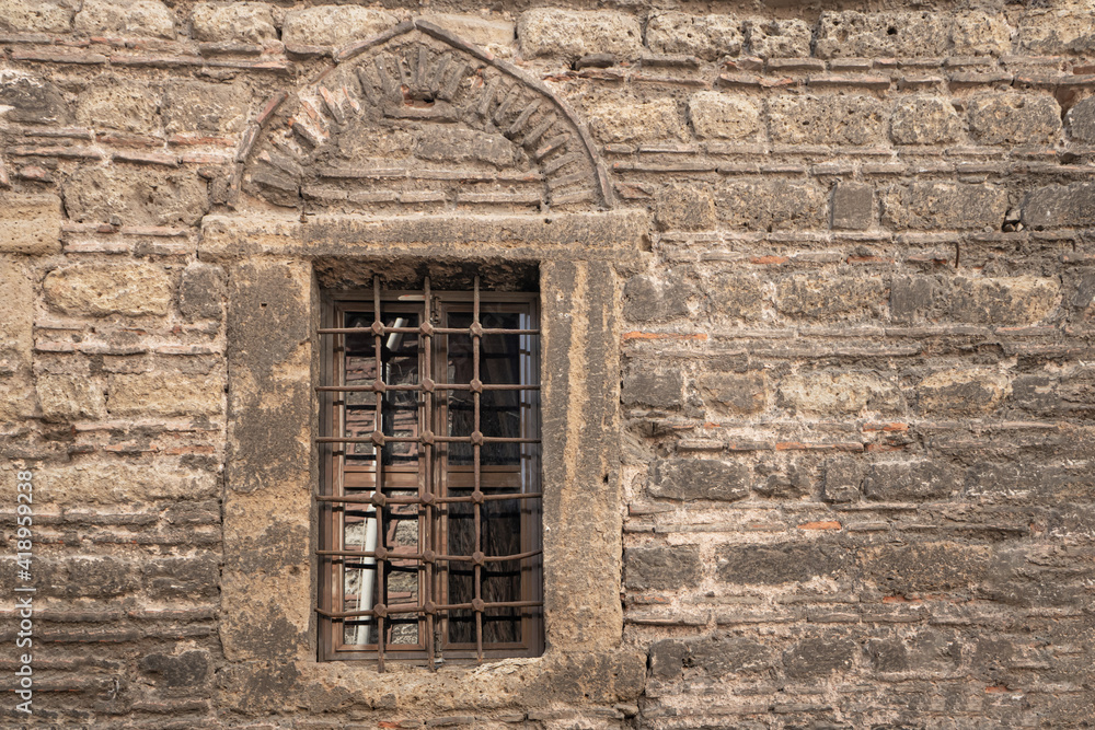 Fototapeta premium Stone wall of an old building, with a grate on the window