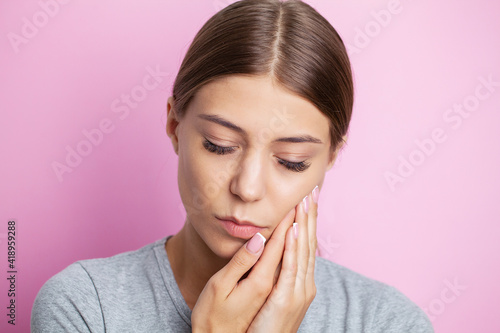 Beautiful young woman suffering from terrible severe toothache, touching cheek with hand.