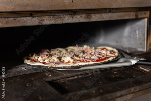 four-cheese pizza is shoveled into a pizzeria oven
