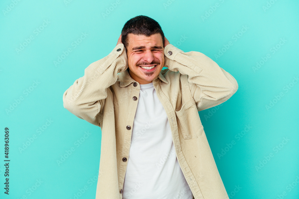 Young caucasian man isolated on blue background covering ears with hands. Young caucasian man isolated on blue background covering ears with hands.