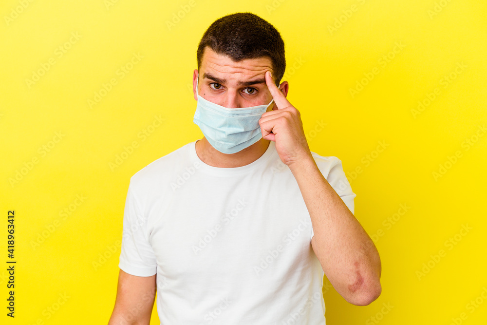 Young caucasian man wearing a protection for coronavirus isolated on yellow background pointing temple with finger, thinking, focused on a task. Young caucasian man wearing a protection for coronavirus isolated on yellow background pointing temple with finger, thinking, focused on a task.
