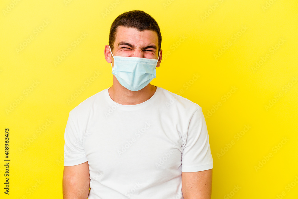 Young caucasian man wearing a protection for coronavirus isolated on yellow background funny and friendly sticking out tongue. Young caucasian man wearing a protection for coronavirus isolated on yellow background funny and friendly sticking out tongue.