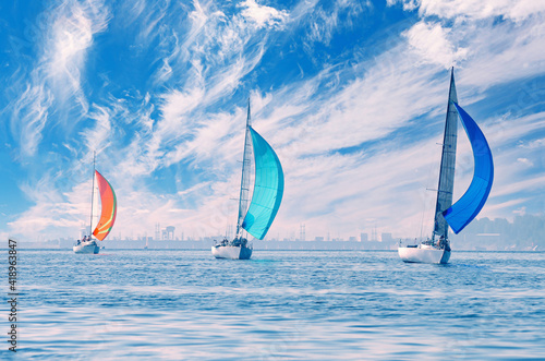 Three sailing yachts sail under a beautiful sky with feathery clouds, the reflection of the sun in the water on the shore is light fog.