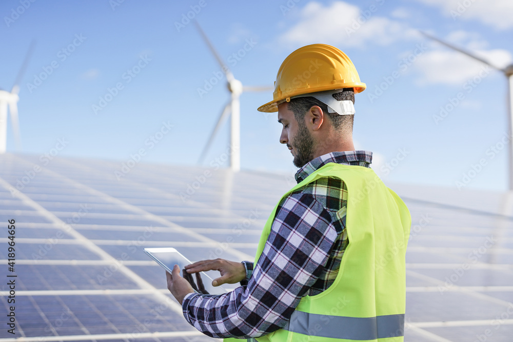 Young man working at solar power station with digital tablet - Renewable energry with wind turbines and solar panels Young man working at solar power station with digital tablet - Renewable energry with wind turbines and solar panels