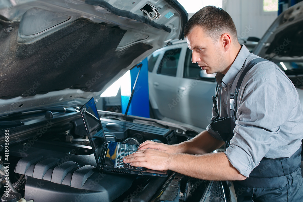 car mechanic using a computer laptop to diagnosing and checking up on car engines parts for fixing and repair. car mechanic using a computer laptop to diagnosing and checking up on car engines parts for fixing and repair.