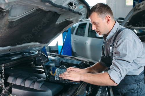 car mechanic using a computer laptop to diagnosing and checking up on car engines parts for fixing and repair.