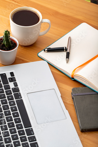 Wooden working desk with laptop computer, smartphone, office supplies and coffee