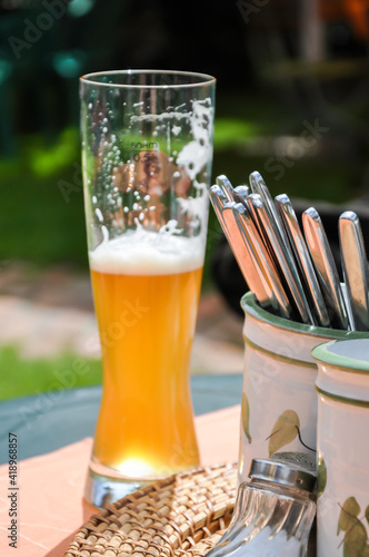 Ein halb geleertes Weißbierglas  auf dem Tisch eines Biergartens, mit Besteck, welches in Bierkrügen steckt. photo